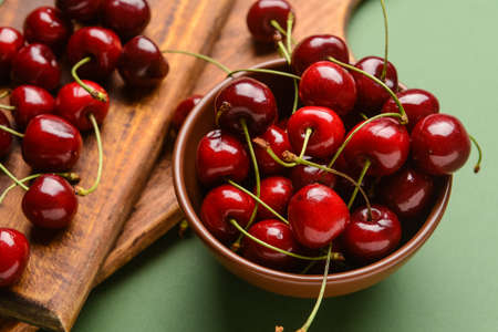 Bowl with sweet cherry on color background