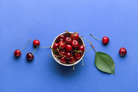 Bowl with sweet cherry on color background