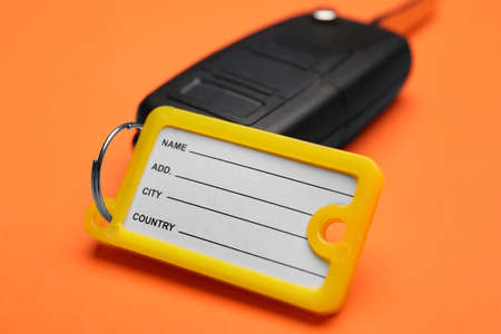 Car key with plastic tag on orange background, closeup