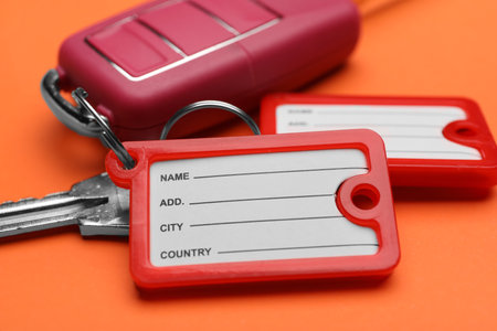 Different keys with plastic tags on orange background, closeup