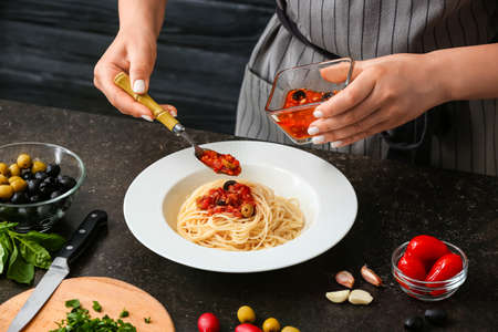 Woman preparing Pasta Puttanesca at kitchen table, closeupの写真素材