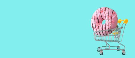 Shopping cart with sweet tasty donut on color background with space for text