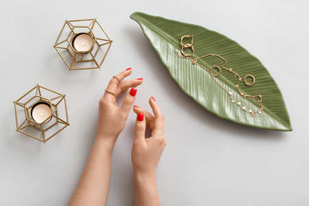Female hands and palm leaf tray with stylish jewelry on light background