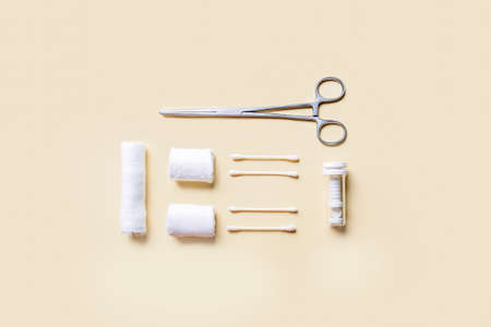 Medical bandage rolls, cotton buds and surgical tool on color background