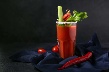 Glass of bloody mary cocktail garnished with celery, cilantro and red chili pepper on dark backgroundの写真素材