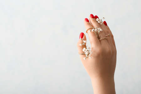 Female hand with stylish rings and gypsophila flowers on light backgroundの写真素材