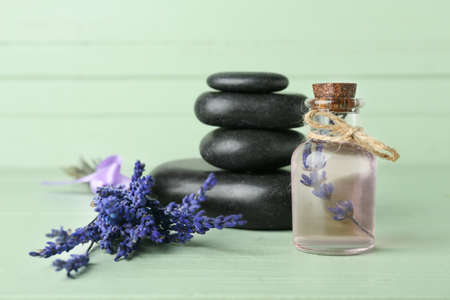 Bottle of lavender essential oil, spa stones and flowers on color wooden backgroundの写真素材
