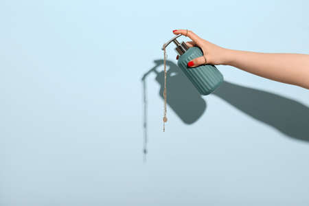 Young woman with beautiful manicure and stylish jewels holding dispenser with cosmetic product on...