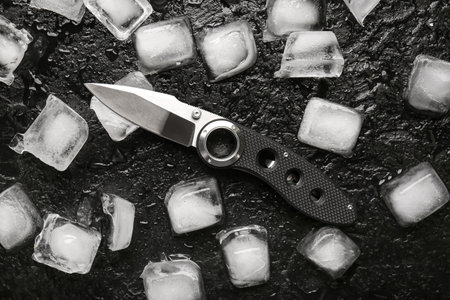 Folding pocket knife with rubberized handle and ice cubes on black textured background