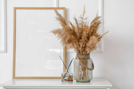 Vase with dry reeds and blank frame on table