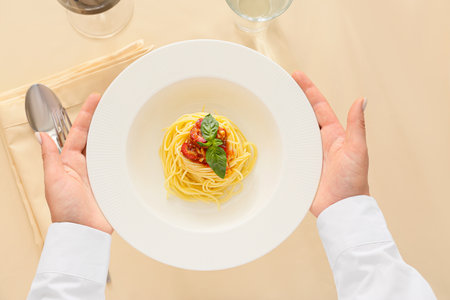 Woman holding plate with tasty Pasta Puttanesca at table in restaurantの写真素材