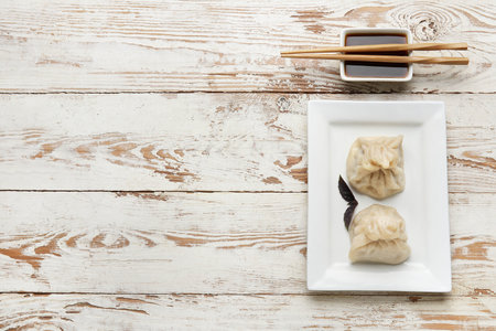 Plate with tasty dumplings, chopsticks and bowl of sauce on light wooden backgroundの写真素材