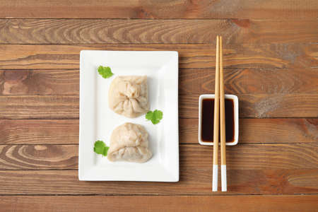 Plate with tasty dumplings, chopsticks and bowl of sauce on wooden background