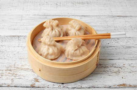 Bamboo steamer with tasty dumplings and chopsticks on light wooden backgroundの写真素材