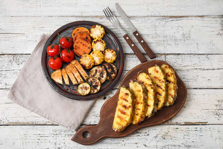 Board with grilled pineapple slices and vegetables on light wooden backgroundの写真素材