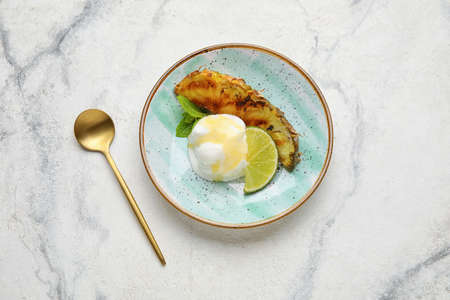 Plate with grilled pineapple slice and ice cream on light backgroundの写真素材
