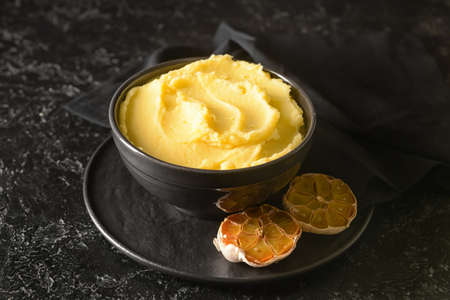 Bowl of tasty mashed potatoes with garlic on dark background