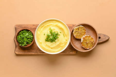 Bowl of tasty mashed potatoes with garlic on color background