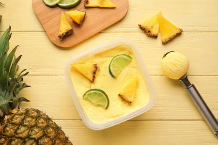 Container with tasty pineapple ice cream on color wooden backgroundの写真素材