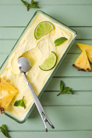 Container with tasty pineapple ice cream on color wooden background