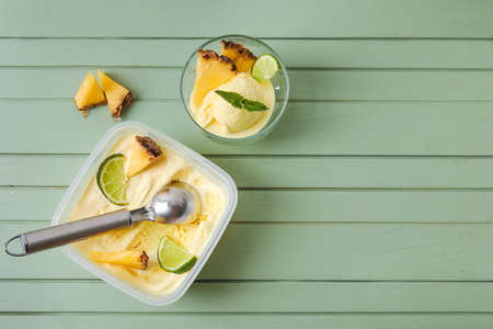 Bowl and container with tasty pineapple ice cream on color wooden background