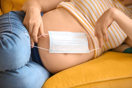 Young pregnant woman with medical mask at home, closeup
