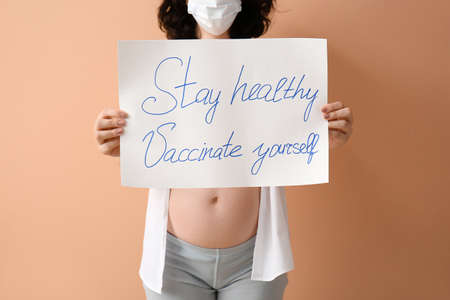 Young pregnant woman holding paper with text STAY HEALTHY - VACCINATE YOURSELF on color backgroundの写真素材