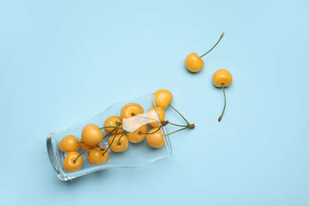 Glass with tasty sweet cherry on color background