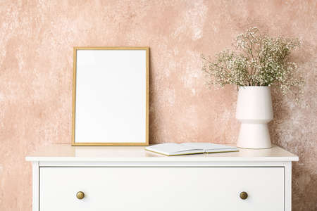 Vase with gypsophila flowers, book and frame on shelf near pink wall