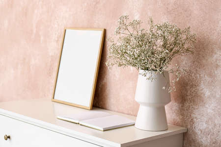 Vase with gypsophila flowers, book and frame on shelf near pink wallの写真素材