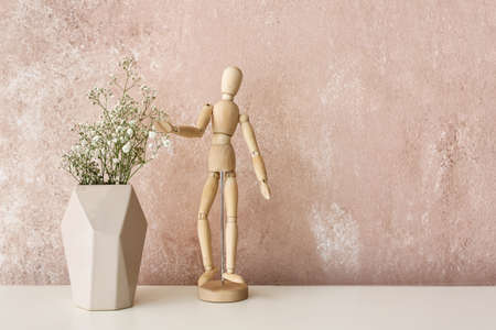 Vase with gypsophila flowers and wooden mannequin on shelf near pink wallの写真素材