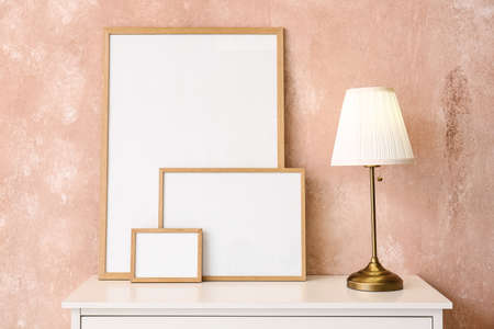 Blank frames and lamp on shelf near pink wall