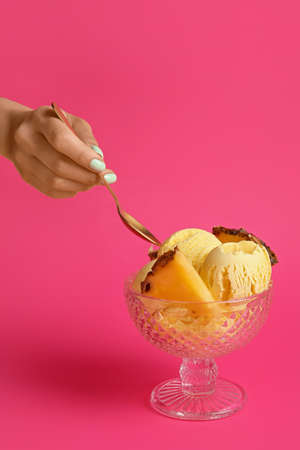 Female hand with tasty pineapple ice cream in glass on color background