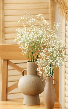 Vases with gypsophila flowers on wooden chair near folding screenの写真素材