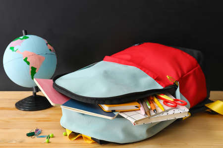School backpack and stationery on table near blackboardの写真素材