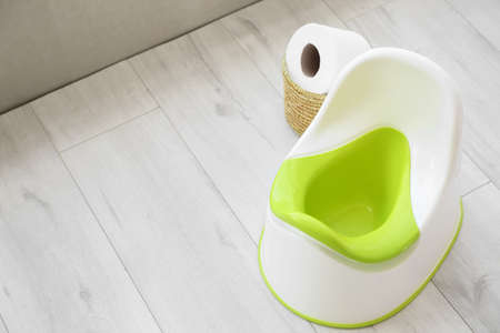 White potty and basket with toilet paper roll on gray wooden floor
