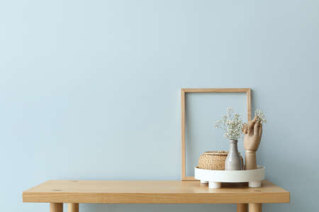 Tray with gypsophila flowers in vase, wooden hand and basket on bench near light wallの写真素材