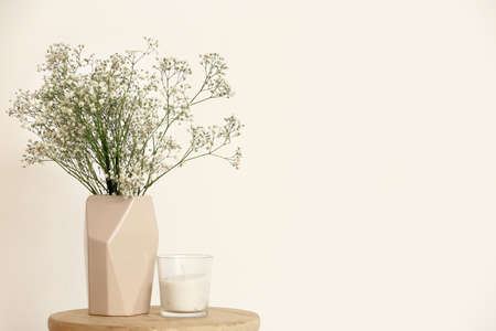 Beige vase with gypsophila flowers and candle on table near light wallの写真素材