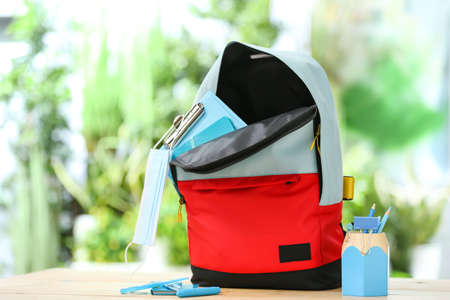 School backpack with stationery and medical mask on table outdoors