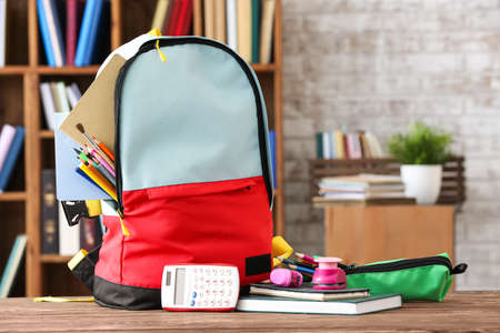School backpack with stationery on table in classroom