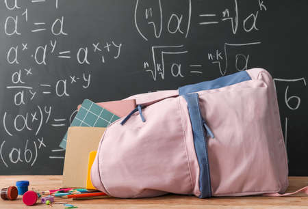 School backpack with stationery on table near blackboard