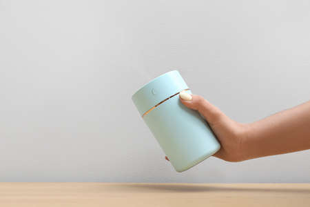 Female hand with modern air humidifier on gray background