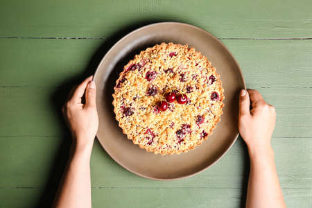 Woman with tasty cherry pie on color wooden background
