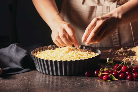 Woman cooking cherry pie at table, closeup