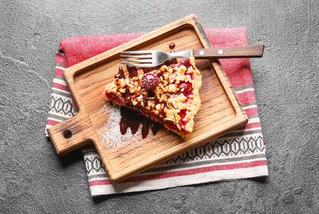Board with piece of tasty cherry pie on gray background