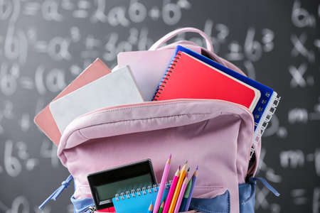 School backpack with stationery against blackboard