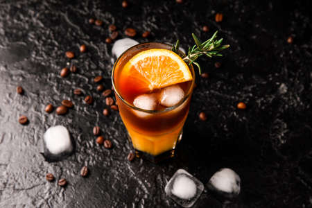 Glass of tasty coffee with orange juice on dark background
