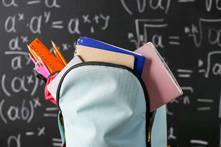 School backpack with stationery against blackboard, closeupの写真素材