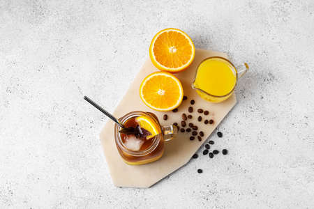 Mason jar of tasty coffee with orange juice and ingredients on light backgroundの写真素材
