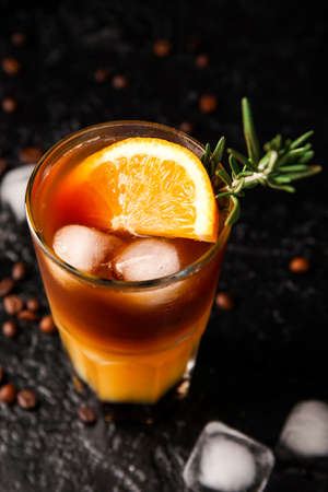 Glass of tasty coffee with orange juice on dark background